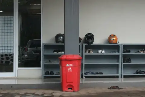 Dustbins: a red garbage can next to a shelf with objects on it