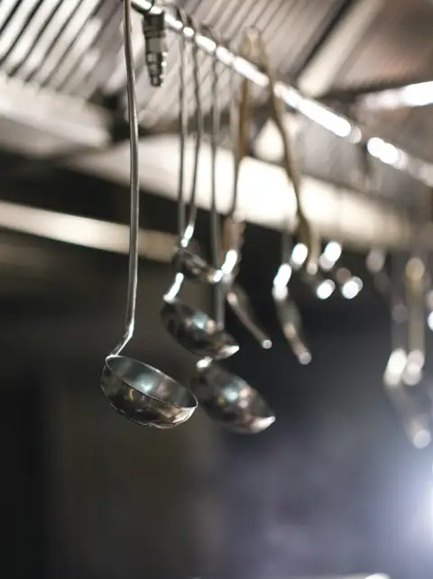 Steel utensils: Metal ladles hanging from a rack in a professional kitchen