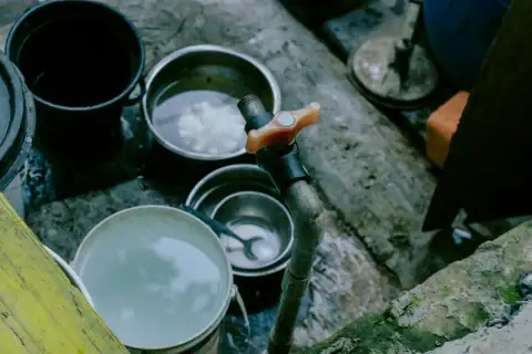 Buckets: Metal buckets and bowls filled with water near a faucet
