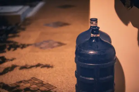 Water campers & jugs: a blue bottle sitting on the floor next to a wall